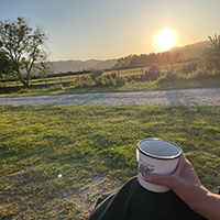 machlud haul yn y pellter a rhywun hefo paned yn ei llaw